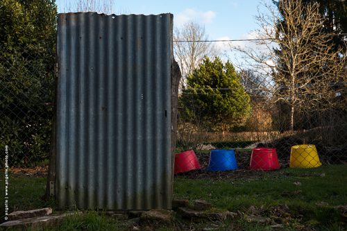 photo © angelle poulaille porte taule ondulee seaux couleurs primaire,grillage jardin rouge bleu jaune étrange alignement